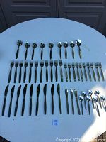 Top view of the entire cutlery set arranged on a white round table showing spoons, forks, knives, and spoons with rounded bowls.