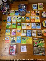 Full spread of assorted Pokemon cards arranged on a table including 2 tin boxes, a large Pokemon chip, stacks of cards, and a small book.