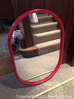 Front view of red plastic framed oval mirror showing vibrant color and clear reflection.