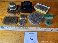 12 vintage pin flower holders arranged on wooden surface with ruler for scale showing variety of sizes and shapes.