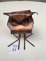 Front view of the small copper owl sculpture showing folded copper metal forming the owl’s face and coiled eyes, standing on metal legs.