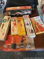 Overall shot of Barbie doll box in black foam insert with five flat packs and a blister-card wig set laid on table