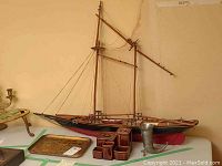 Photo showing wooden Bluenose model sailboat, pewter horn, decorative tray, and brown ceramic coffee and tea service items arranged together on a table.
