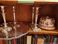 Four silver plated candlesticks and large silver plated serving tray with vintage covered cheese keeper on wooden shelf