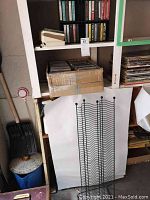 CD tower rack standing on floor with cardboard box of CDs on one shelf, cassette tapes in upper cubby slots