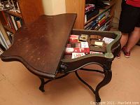 Side view of vintage oak demi-lune game table with hinged top partly open showing interior storage and game board
