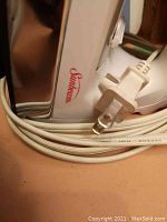 Close up of Sunbeam iron brand logo and power cord plug, white plastic housing with wrapped cord.