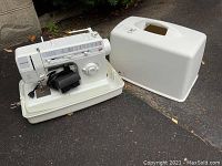 Singer portable sewing machine Model 9818C with white carrying case placed outdoors on pavement. Machine shown with power cord and foot pedal coiled inside base cover.