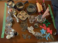 Top-down view of all toy baking items laid out on a surface including kettle, pans, rolling pins, measuring cups, cookie cutters and more