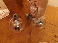 Two vintage Aerolux Kayatt glow bulbs with floral figural neon designs inside clear glass, displayed on a wood surface.