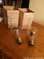 Two Aerolux Kayatt figural neon glow bulbs with original cardboard boxes on wooden surface