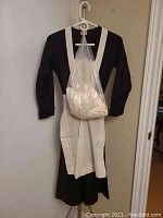 Full-length shot of black maid's dress with white apron and collar hanging on a hanger on a door.