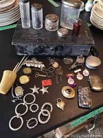 Overall lot on black surface showing glass jars, metal box, watches, jewelry, medallions, and cases