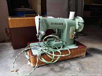 Side angled view of vintage green Singer sewing machine model 185J with brown tan case and attached cords