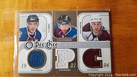 Front of the card showing portraits of Joe Sakic, Peter Forsberg, and Ryan Smyth, each with a game-worn jersey piece in die-cut windows colored blue, white, and maroon respectively.