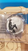 Silver coin in plastic case featuring Superman design with '2015' and purity inscriptions visible.