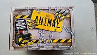 Front and top close-up image showing The Animal Monster Truck toy box with chain and claw detail graphics and warning text.