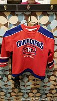 Front view of red Montreal Canadiens child size 6X jersey hanging on hanger showing logo, text and striped design.