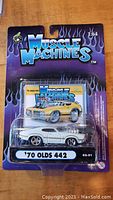 Front view of unopened Muscle Machines 1:64 '70 Olds 442 model car in blister pack showing packaging and branded backing card