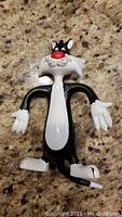 Front view of a black and white bendable Sylvester the Cat figure with a red nose, white gloves, belly, and feet on a granite surface.
