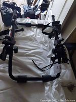 Top-down view of black metal bike rack with padded support and straps, placed on white surface.