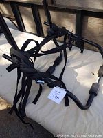 Photo showing black metal bike rack with multiple securing straps and padded support bars placed on a beige fabric surface.