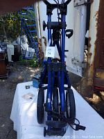 Front view of the blue Sun Mountain golf push cart folded upright showing the three wheels and handle detail.