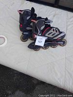 Pair of children's inline rollerblades size 4, black and gray with red accents, four wheels each arrangement, placed on a light colored surface.