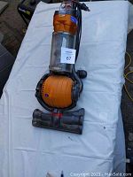 Photo of Dyson DC24 upright vacuum cleaner on white cloth, showing full unit from top with dust bin and floor cleaning head visible.