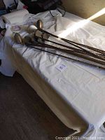 Nine Select golf clubs on a white table, including six irons and three woods with filament wound graphite shafts.