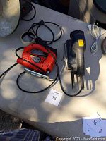 Photo showing electric jigsaw and detail sander side by side on a table, both with attached power cords.