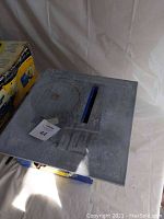 Top view of the MasterCut tile saw work surface showing metal table and circular saw blade under dust or residue.