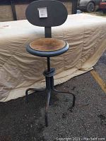 View of metal swiveling shop chair showing wooden seat and metal backrest against outdoor backdrop.