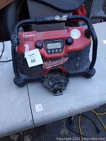 Front view of Milwaukee job site radio showing control knobs, digital display, speaker grill, and battery slot at the base.