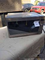 Panasonic microwave oven on a cloth-covered surface outdoors, showing front and right side with label 144.