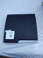 Black PlayStation 3 Slim console top view with a MaxSold lot number sticker.