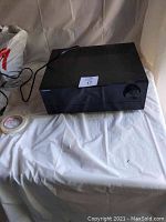 Black Samsung stereo receiver viewed from front and angle, sitting on a white surface with power cord visible.