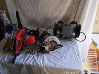 Four tools on a white backdrop showing the bench grinder, a Craftsman handheld circular saw, a red and silver compound miter saw, and another smaller saw.