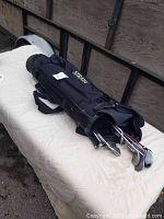 Black Strata branded golf bag with several golf clubs partially visible inside, laid on a beige surface.