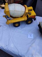 Metal yellow Tonka cement mixer toy with white barrel and black and yellow wheels on white cloth.