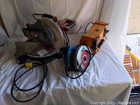 Photo of the Makita circular saw, miter saw, and Mastercraft bench grinder placed on a white sheeted surface, angled to show power cords and tool condition.