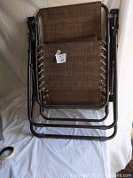 Two brown anti gravity folding chairs stacked, showing woven fabric and metal frames.