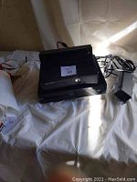 Xbox One console showing top vents, power button, and Xbox logo in black, with cables.