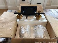 View of double pendant light fixture in box showing black base, gold mounts and two wrapped glass pendant shades.