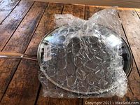 Frying pan with glass lid partially wrapped in bubble wrap, showing shiny reflective surface and metal handle.