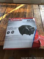 Packaged brand new Coleman NXT RoadTrip grill cover with full product labeling showing weather resistance and UV protection details.
