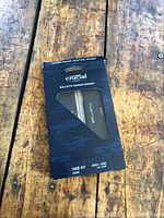 Two photos of two boxed Crucial Ballistix DDR4-3200 memory modules on a wooden surface.