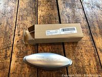 Photo showing a silver oval Quartet dry eraser next to a brown cardboard box on a wooden surface.