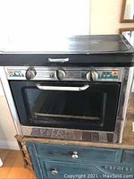 Front view of dual burner stove and small oven with closed top lid and control knobs visible.