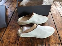 Pair of white leather women's slippers with tan trim, slip-on style, shown beside and inside the original black brand box with Ecco logo.